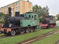 Dwa zabytkowe parowozy, zielony i rudy, stoją na torach przy budynku. To część ekspozycji muzeum kolei wąskotorowej w Sochaczewie.