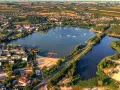 Widok z lotu ptaka na zalew Mrożyczka, z wakeboardzistami, plażą i otaczającą zielenią.