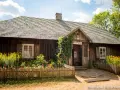 Drewniana apteka w Muzeum Wsi Kieleckiej, otoczona kwitnącym ogrodem i ogrodzona płotkiem.
