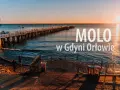 Zachód słońca nad morzem, długie molo w Orłowie, ludzie spacerują po plaży.