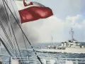 ORP Wicher płynie po wzburzonym morzu. Na pierwszym planie widać fragment statku i polską flagę.