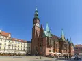 Rynek we Wrocławiu z Ratuszem, gdzie mieści się muzeum sztuki mieszczańskiej. Wokół kawiarnie i ludzie spacerujący.