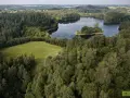 Malownicze jezioro Jaczno otoczone gęstym lasem, z małą wyspą pośrodku. W oddali widać pagórkowaty krajobraz pól i kolejnych lasów.