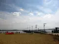 Plaża nad jeziorem Miedwie, z molo i spacerującymi ludźmi. Słoneczny dzień, chmury na niebie.