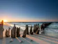 Zachód słońca nad Bałtykiem. Drewniane pale, pozostałości dawnych falochronów, tworzą malowniczy krajobraz na plaży. Idealne miejsce dla miłośników nadmorskich miejscowości.