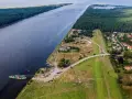 Widok na Wisłę i jej ujście. Prom przewozi samochody, a w oddali widać las i zabudowania.