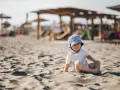 Uroczy maluch w pasiastym kapelusiku na plaży. Idealne miejsce, gdzie na wakacje z rocznym dzieckiem, by cieszyć się słońcem i piaskiem.