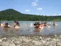 Dzieci pluskają się w jeziorze, świetny pomysł na wakacje! W tle zielone wzgórza i błękitne niebo.