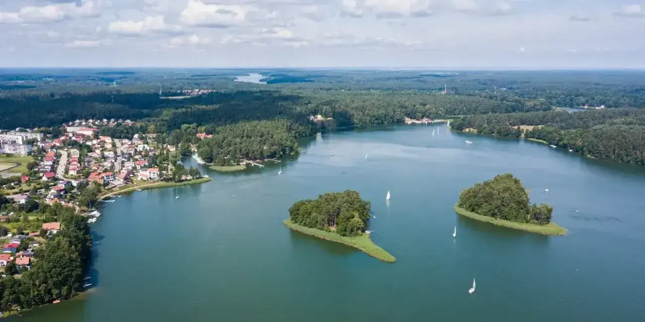 Malownicze jezioro z wyspami i żaglówkami, otoczone lasem i zabudowaniami. To widok, który potwierdza, że to jedne z najpiękniejszych jezior w Polsce.