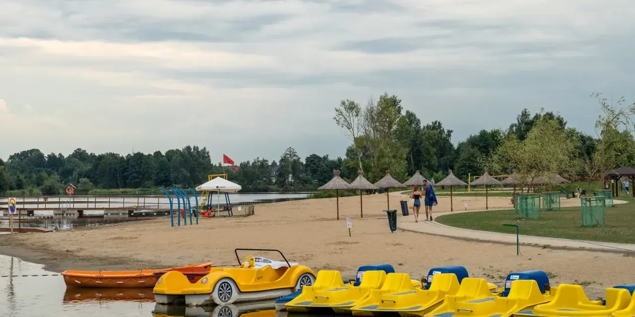 Żółte rowerki wodne i łódki czekają na plaży. Idealne miejsce na wypoczynek, jak na Mazurach blisko Warszawy.