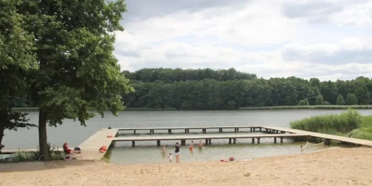 Plaża nad jeziorem Zaleskim z drewnianymi pomostami, na których bawią się ludzie.