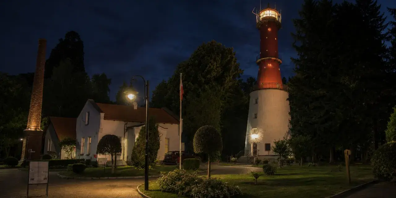 Nocna panorama latarni morskiej Rozewie z oświetloną wieżą i budynkami.