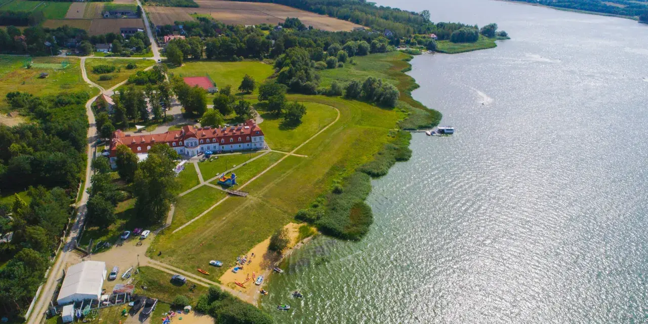 Widok z lotu ptaka na **zalew domaniow** z hotelem, plażą, kajakami i łodziami.
