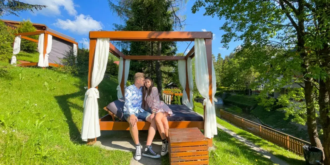 Para zakochanych na łóżku pod baldachimem, idealny pomysł na weekend w otoczeniu zieleni i strumyka.