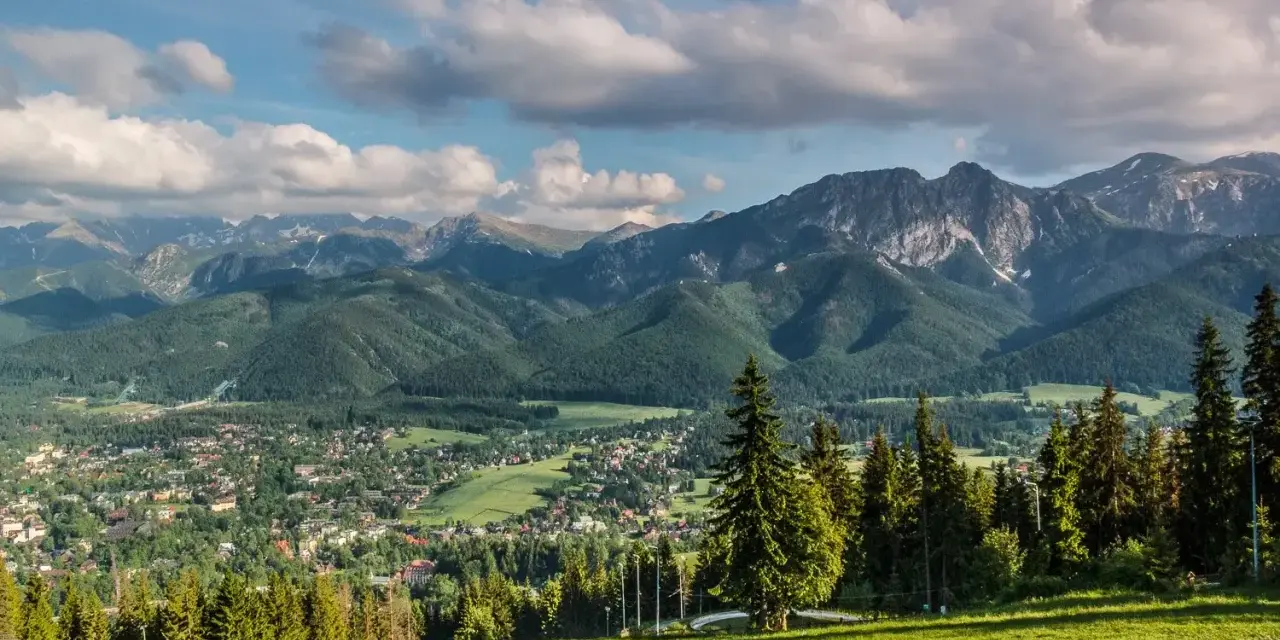 Widok na Tatry z Zakopanem u podnóża. W oddali widać skaliste szczyty, a bliżej zielone zbocza porośnięte lasem. To właśnie takie krajobrazy tworzą regle.