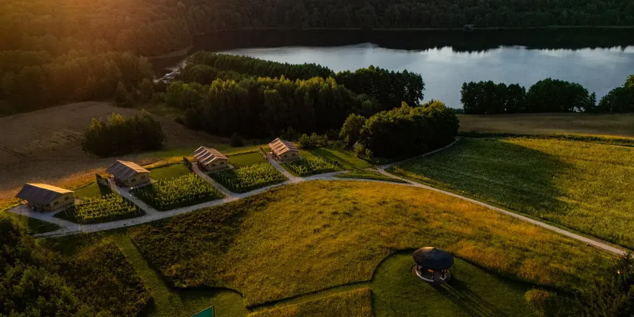 Malownicze domki nad jeziorem, idealne na fajne miejsca na wakacje. Słońce zachodzi, rzucając złote światło na pola i lasy.