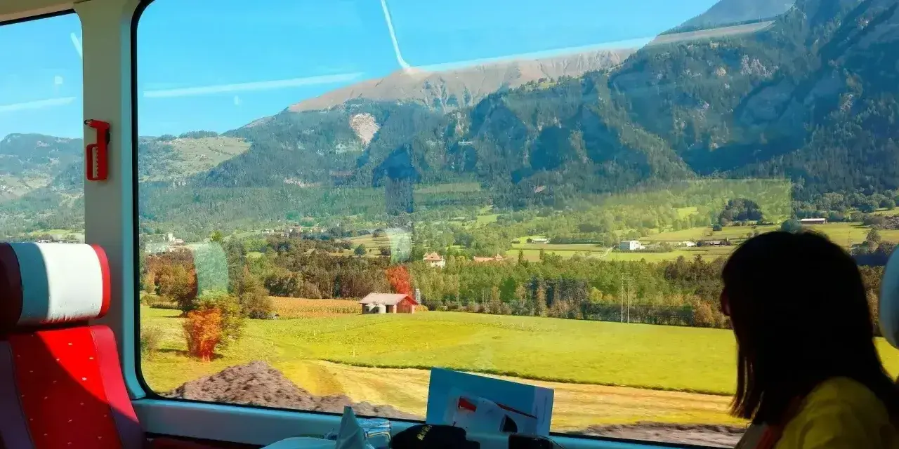 Widok z okna pociągu podczas wycieczki objazdowej. Zielone doliny, góry i domki.