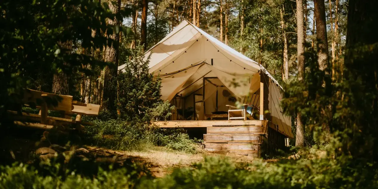 Namiot na Mazurach, otoczony lasem. Drewniana ławka i taras zapraszają do odpoczynku. Idealne miejsce na mazury pod namiot.