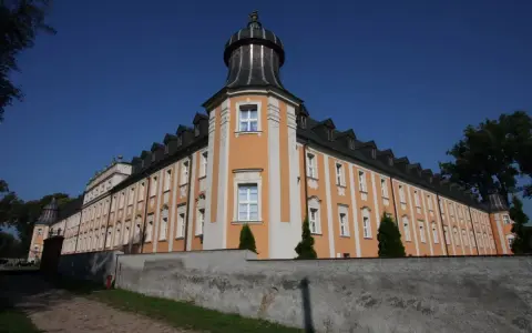 Klasztor Paradyż, okazały budynek z pomarańczowo-białą fasadą i wieżyczką, otoczony murem.