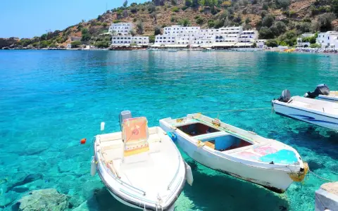 Idealne miejsce, gdzie pojechać na wakacje: białe domki na wzgórzu, turkusowa woda i łódki kołyszące się przy brzegu.