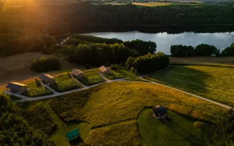 Malownicze domki nad jeziorem, idealne na fajne miejsca na wakacje. Słońce zachodzi, rzucając złote światło na pola i lasy.