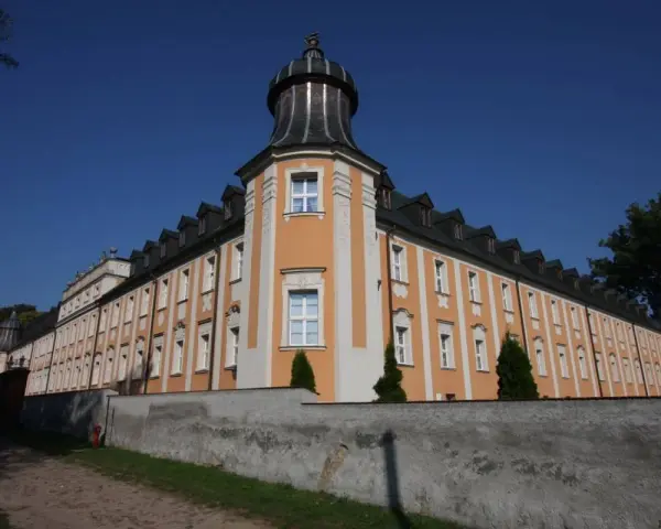 Klasztor Paradyż, okazały budynek z pomarańczowo-białą fasadą i wieżyczką, otoczony murem.