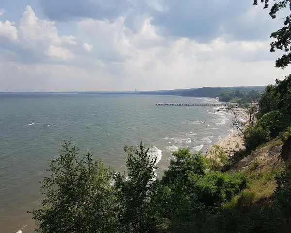 Widok z klifu orłowskiego na morze, plażę z ludźmi i molo. W oddali widać zarys wybrzeża.