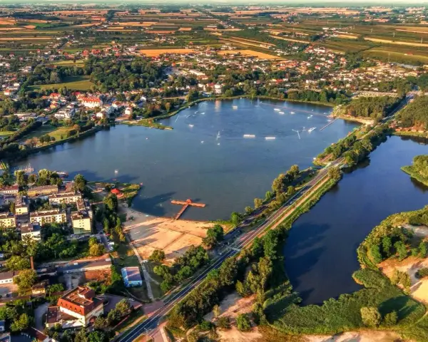 Widok z lotu ptaka na zalew Mrożyczka, z wakeboardzistami, plażą i otaczającą zielenią.