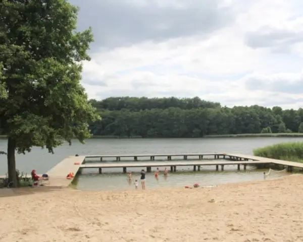 Plaża nad jeziorem Zaleskim z drewnianymi pomostami, na których bawią się ludzie.