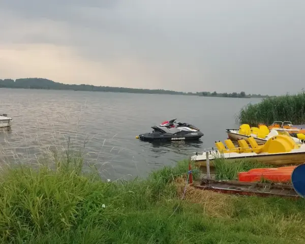Na jeziorze Paczkowskim pływa motorówka i skutery wodne. Na brzegu czekają rowery wodne i kajaki.