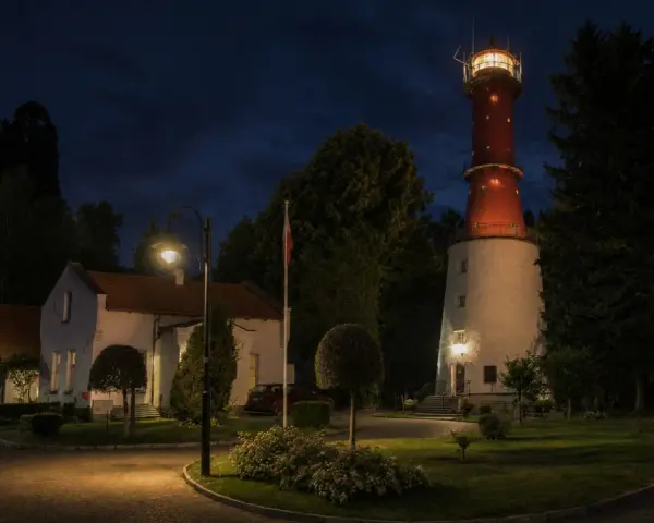 Nocna panorama latarni morskiej Rozewie z oświetloną wieżą i budynkami.