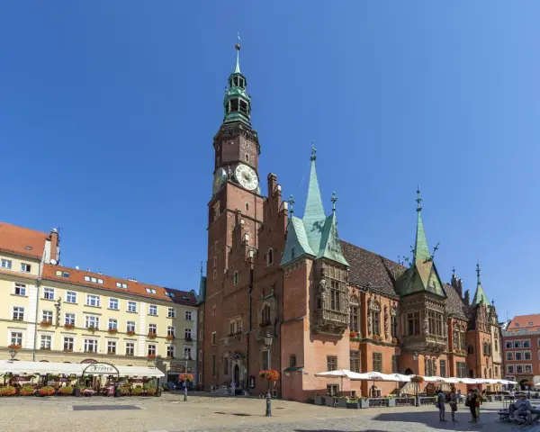 Rynek we Wrocławiu z Ratuszem, gdzie mieści się muzeum sztuki mieszczańskiej. Wokół kawiarnie i ludzie spacerujący.