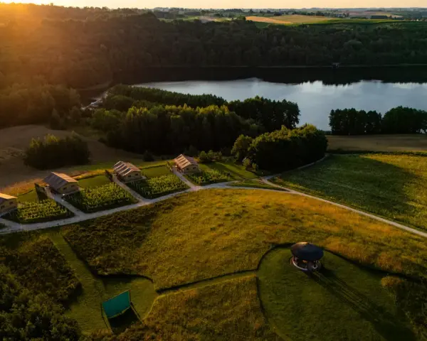 Malownicze domki nad jeziorem, idealne na fajne miejsca na wakacje. Słońce zachodzi, rzucając złote światło na pola i lasy.