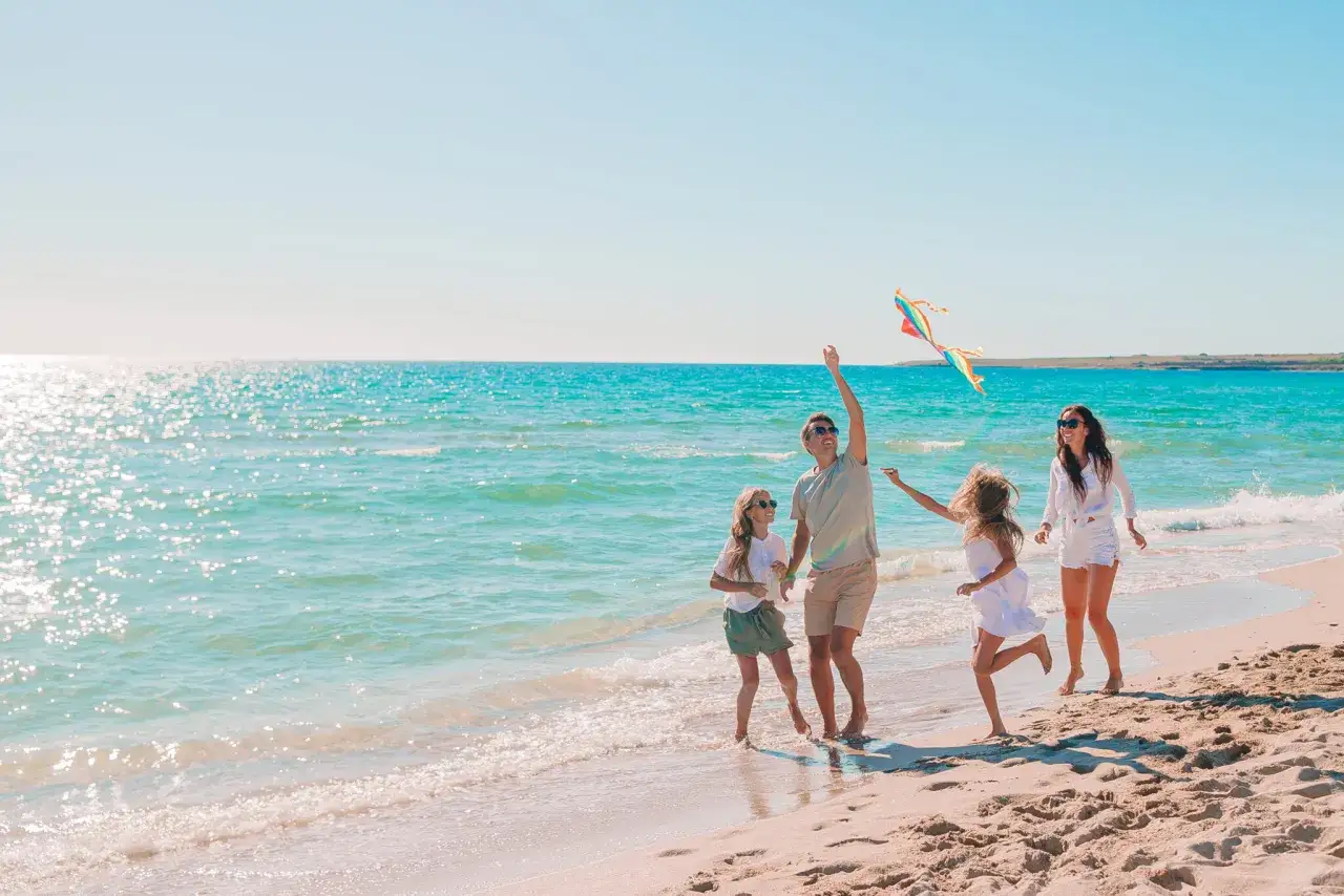 Szczęśliwa rodzina puszcza latawiec na plaży. Idealne wakacje z dziećmi nad turkusowym morzem.