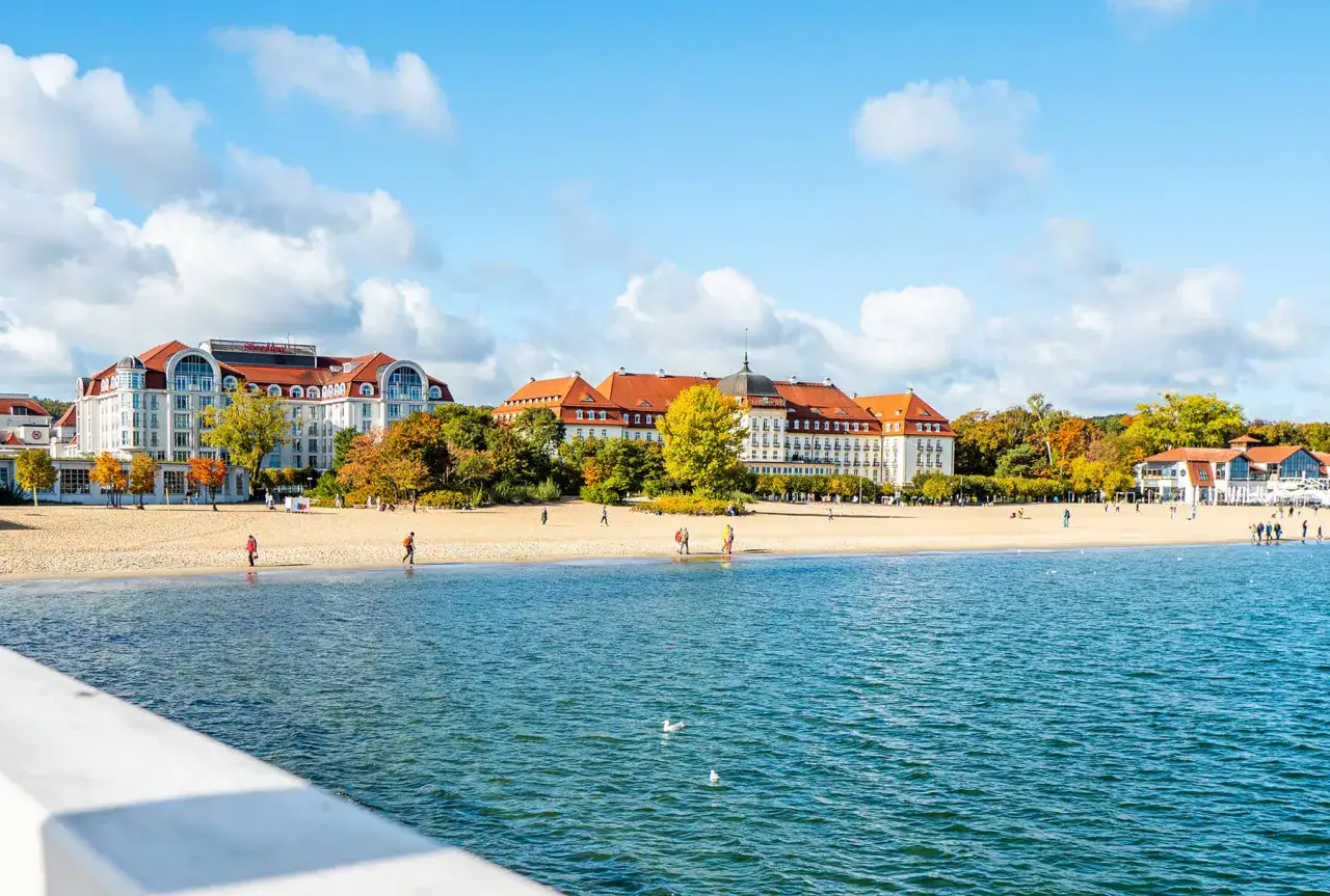 Piękne miejscowości nad morzem jesienią. Plaża z kilkoma spacerującymi osobami i imponujące budynki hotelowe w tle.