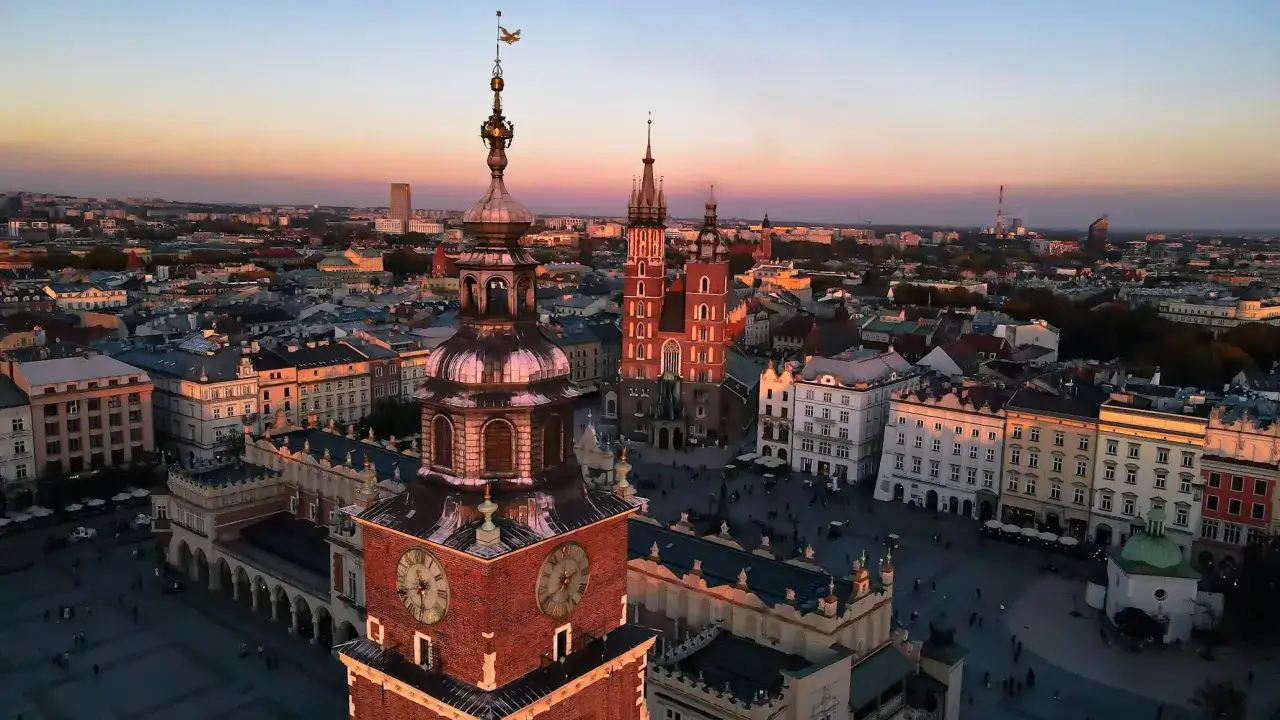 Zachód słońca nad Rynkiem Głównym w Krakowie. Idealne miejsce na city break, z Wieżą Ratuszową i Kościołem Mariackim w tle.
